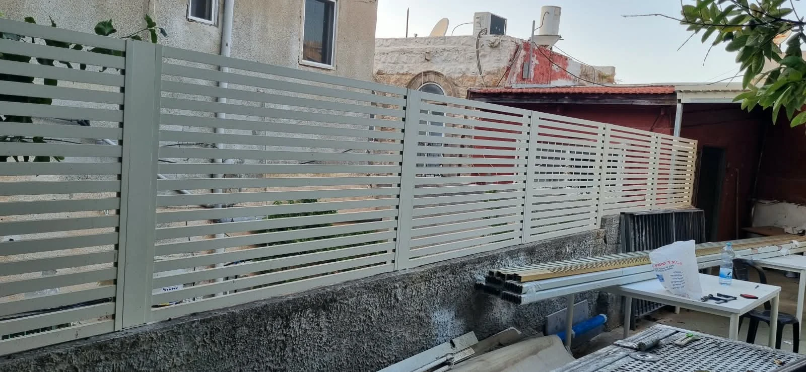 גדר פסים בהירה על גבי קיר נמוך, בזמן התקנה — ענק הצל